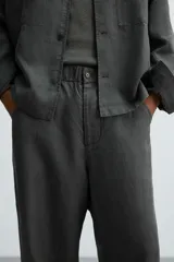 Pantalón de corte relajado confeccionado en tejido de cáñamo color blanco roto. Presenta cintura elástica con cordón interior ajustable, cierre frontal con botones, bolsillos laterales y un bolsillo trasero de plastrón.