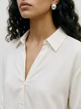 Camisa de manga larga en color blanco, con cuello camisero y cierre frontal de botones.