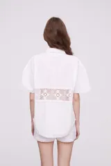 Camisa blanca de algodón con apliques de crochet calado en la cintura, manga corta y cuello camisa.