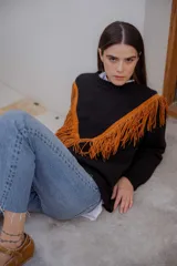 Sweater tejido de lana color negro con diseño de flecos de gamuza en tono tostado en la parte frontal, formando una silueta en V. Presenta cuello redondo y mangas largas.