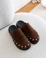 Zuecos de ante color beige con diseño destalonado, punta redonda y tachas metálicas plateadas alrededor de la suela.