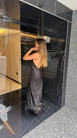 Vestido largo negro con escote halter cruzado y abertura frontal. El ruedo presenta un detalle de flecos.