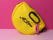 Monedero triangular de color amarillo con diseño de carita feliz bordada en negro. Incluye un mosquetón negro y un tirador de cierre de silicona en color fucsia.