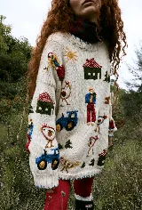 Buzo tejido de lana merino color crema, con diseño bordado a mano que representa escenas de granja, incluyendo figuras de granjeros, casas, tractores y animales. Presenta un corte holgado y cuello redondo.