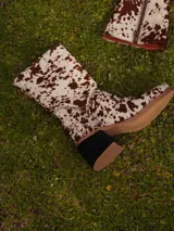 Botas de caña media con estampado animal print tipo vaca, taco ancho y punta redondeada. Cuenta con cierre lateral y diseño de pelo sintético.
