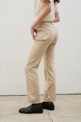 Pantalón de denim negro con diseño de tachas metálicas distribuidas en patrones curvos. Presenta un corte recto y tiro medio.