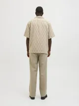 Camisa de manga corta Jack & Jones con cuello resort y cierre de botones. Diseño con estampado de espiga en tonos beige y blanco. Confeccionada en tejido dobby 100% algodón.