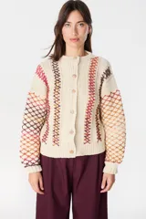 Saco de punto artesanal en color crudo, con diseño de red multicolor en mangas y laterales. Presenta cuello redondo, cierre frontal con botones y puños acanalados.