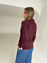 Polera de tejido de punto color bordeaux con cuello semi volcado. Presenta un diseño de ochos en el frente, mientras que las mangas y la espalda son lisas.