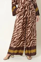 Pantalón palazzo de tiro alto con cintura elastizada y bolsillos laterales. Presenta un estampado de cebra en tonos marrón oscuro y beige claro, con un borde inferior en marrón liso y una franja mostaza/verde oliva.