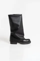 Botas de caña alta confeccionadas en ecocuero negro, con diseño holgado y suela plana con plataforma baja.