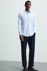 Camisa de manga larga, color celeste con finas rayas verticales blancas, cuello italiano y cierre frontal de botones.