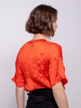 Blusa de manga corta con escote en V, confeccionada en tela satinada con textura de pliegues horizontales.