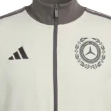 Campera deportiva Adidas AMG Petronas Silver Arrows Icon F1, color blanco crudo con detalles en gris oscuro, cuello alto, cierre frontal completo y bolsillos laterales. Presenta el logo de Adidas y el escudo de Mercedes-AMG Petronas.