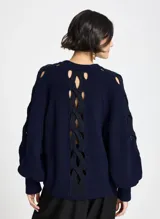 Sweater de punto color azul marino con diseño de aberturas entrelazadas en el frente y a lo largo de las mangas. Presenta cuello redondo, mangas largas con puños ajustados y un corte holgado.