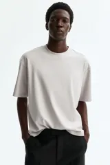 Remera boxy de algodón pesado, color gris claro, con cuello redondo ribeteado acanalado, hombros caídos y mangas cortas.