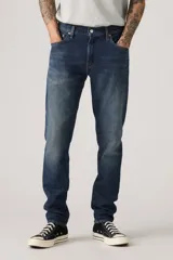 Pantalón de jean azul oscuro, corte slim fit, con pierna cónica y tiro medio. Diseño clásico de cinco bolsillos.