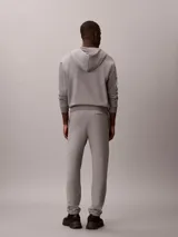 Pantalón jogger gris melange de felpa Calvin Klein, con cintura elástica, bolsillos laterales y puños acanalados. Cuenta con el monograma CK bordado discretamente en la pierna.