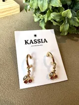 Aros dorados tipo argolla con dije de cerezas rojas y hojas blancas.