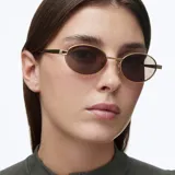 Lentes de sol con montura ovalada de acero inoxidable en color dorado y cristales polarizados en tono marrón. Presentan un diseño minimalista con patillas de acetato negro.