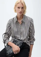 Camisa de manga larga con estampado de rayas verticales en blanco y negro, cuello camisero y cierre frontal con botones ocultos. Diseño recto y tejido fluido.