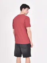 Remera de corte regular en color gris oscuro jaspeado, con cuello redondo y mangas cortas. Presenta un estampado frontal con diseño gráfico estilo veraniego que incluye palmeras y texto.