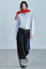 Jeans de tiro bajo y pernera ancha, confeccionados en denim azul oscuro con pespuntes en contraste. Cuentan con un diseño de cinco bolsillos, cierre frontal con cremallera y botón metálico, y destacan por su amplio doblando en el bajo que deja ver el revés de la tela con detalles de costura selvedge.