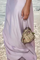 Bolso rígido con estructura metálica dorada y forro interior de tela color beige ajustable con lazada. Decorado con charms colgantes de diferentes motivos y asa superior rígida.