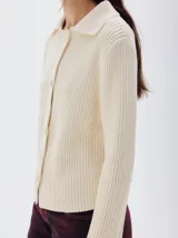 Cardigan de punto acanalado color crema, con cuello polo, cierre frontal de botones tejidos y manga larga.