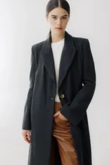 Tapado largo de paño en color beige, con solapas clásicas, cierre frontal de dos botones y corte recto estructurado.