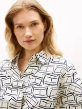 Camisa Tommy Hilfiger de corte amplio confeccionada en lino puro, con diseño estampado de líneas geométricas en azul sobre base blanca. Presenta cuello inglés, cierre frontal abotonado, mangas largas con puños abotonados y logo bordado en el pecho.