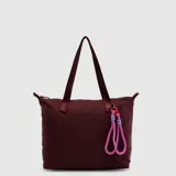 Bolso tipo tote bag color bordó con asas de hombro fijas de cinta estampada y un llavero decorativo de cuerdas color rosado y violeta con mosquetón rojo. Cuenta con cierre principal y el logo de la marca impreso al frente.