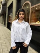 Camisa blanca de manga larga con sutiles rayas verticales, cuello camisero, cierre frontal con botones y dos bolsillos frontales con solapa.