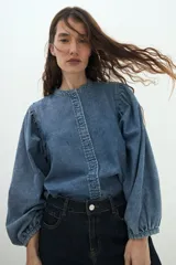 Camisa de jean de corte clásico con cuello mao, cierre frontal con botones y mangas largas abullonadas con puños elásticos.