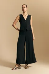 Pantalón negro de corte ancho y silueta fluida, con cintura elastizada y pretina ancha con botones metalizados irregulares.