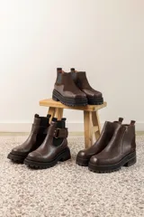 Botas cortas negras con plataforma dentada, confeccionadas en una combinación de cuero con textura de reptil y paneles de gamuza. Presentan un cierre frontal metálico y puntera cuadrada.