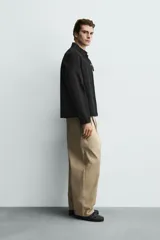 Sobrecamisa negra de corte relajado, confeccionada en tejido con mezcla de algodón elástico. Presenta cuello solapa, cierre frontal de cremallera, bolsillos de plastrón en el pecho y bolsillos de vivo en la cadera.