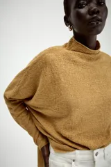 Jersey de punto con textura, color crudo, de cuello subido y manga larga. Presenta un diseño holgado con bajo asimétrico y aberturas laterales.