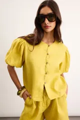 Blusa de lino color amarillo, con cuello redondo, mangas cortas abullonadas y cierre frontal con botones.
