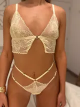 Conjunto de lencería de encaje color champagne, compuesto por un bralette estilo top con cierre frontal de gancho y breteles regulables, y una tanga de tiro alto con tiras laterales ajustables.
