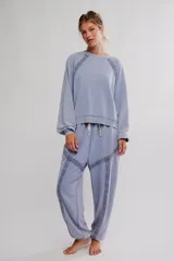 Conjunto de pijama de frisa lavada color celeste, compuesto por un buzo de calce amplio con escote redondo, mangas raglán abullonadas y puntilla aplicada sobre las costuras, y un pantalón de cintura elastizada con cordón, puños en los tobillos y detalles de puntilla en los paneles.