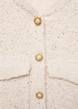 Chaleco color crema con textura tweed, cuello redondo, cierre frontal con botones dorados y dos bolsillos de parche con botón.