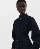 Camisa de denim azul oscuro, con cuello camisero, cierre frontal con botones y mangas largas ajustadas.