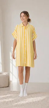 Vestido camisero de silueta relajada, con cuello clásico, cierre frontal de botones y mangas cortas. Presenta un diseño de rayas verticales en colores amarillo y blanco.
