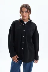 Sobrecamisa de jean color negro, con corte oversize, cuello camisero, cierre frontal con botones metálicos y bolsillos frontales con solapa.