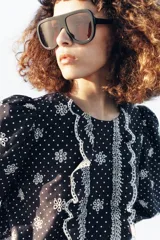 Blusa azul marino con estampado de lunares blancos, cuello redondo y mangas abullonadas. Presenta detalles de bordados perforados, volantes delanteros y acabados elásticos.