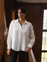 Camisa de color beige con cuello clásico y cierre frontal de botones. Presenta un diseño de bordado lineal en color blanco que recorre las mangas largas.
