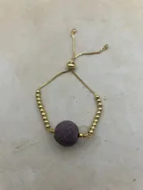 Pulsera dorada con tres piedras volcánicas negras y cierre corredizo.
