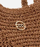 Bolso de playa tejido en fibra de papel color marrón claro, con asas medianas y detalle de logo metálico dorado en el centro.
