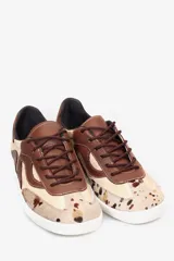 Championes de cuero con diseño de paneles orgánicos en tonos tierra. Presenta una combinación de cuero liso marrón y beige, con detalle de cuero con pelo estampado tipo vaca en la puntera. Cuenta con cordones al tono y suela blanca.